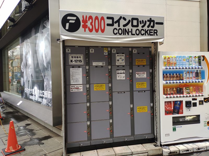 駅の外：北口カラオケ店のビルの角にあるコインロッカー